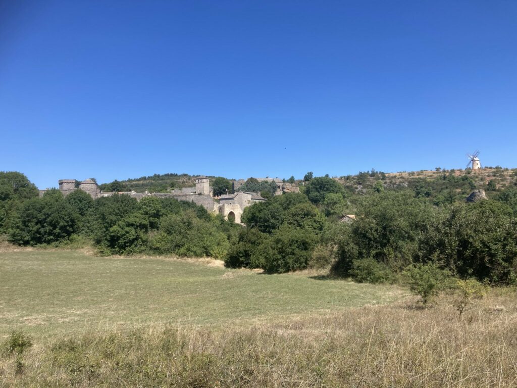 Photo de murailles au milieu d'arbres. Ciel très bleu. A droite, au loin, on voit un grand moulin